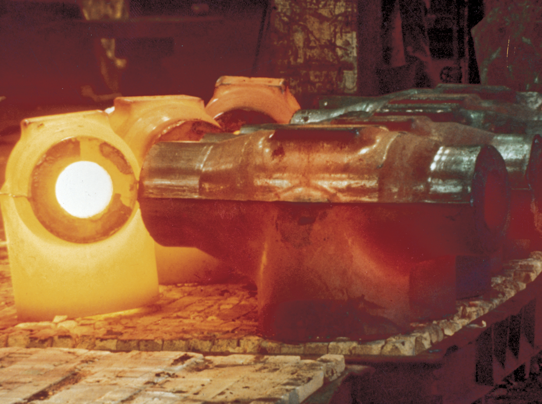 Du métal en fusion rougeoie et orange à l'intérieur d'un four industriel, entouré de grands moules métalliques absorbant la chaleur. La scène est illuminée par la lumière intense émise par le métal chaud.