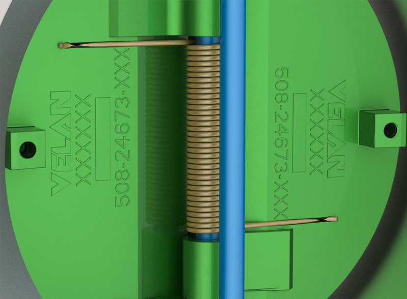 Close-up of a green, circular mechanical component with "VELAN XXXXX" and "508-24673-XXX" engraved on it. A coiled spring and two rods are visible along the central axis.